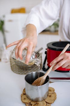 Close-up of craftswoman's hands pouring wax into a pot, captured in a modern workshop.